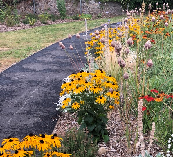 Photo of a tarmac path with a colourfyl flower bed of yellow and red flowers